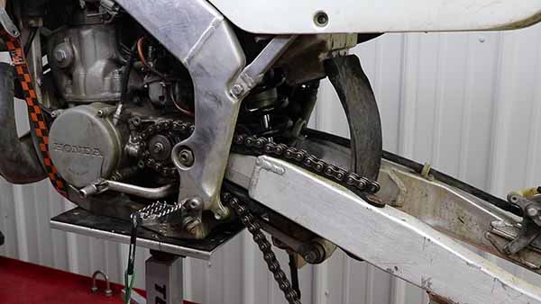 Run your chain through the guides, so the ends meet on top of the swingarm.